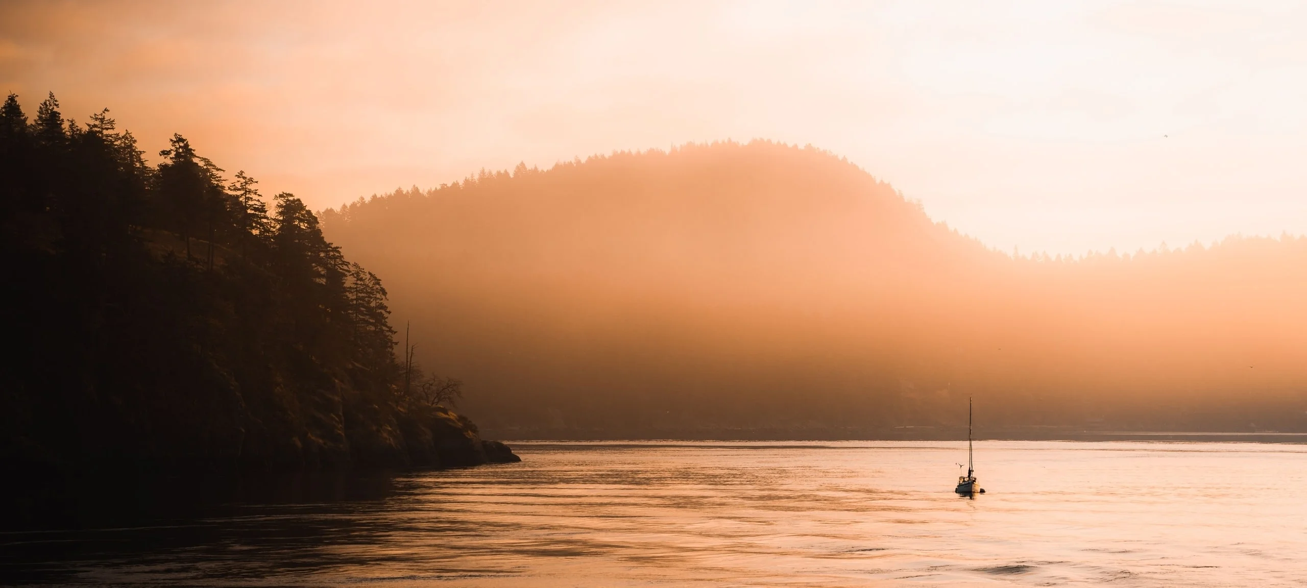 Orange sunrise over ocean around the Gulf Islands, with sailboat
