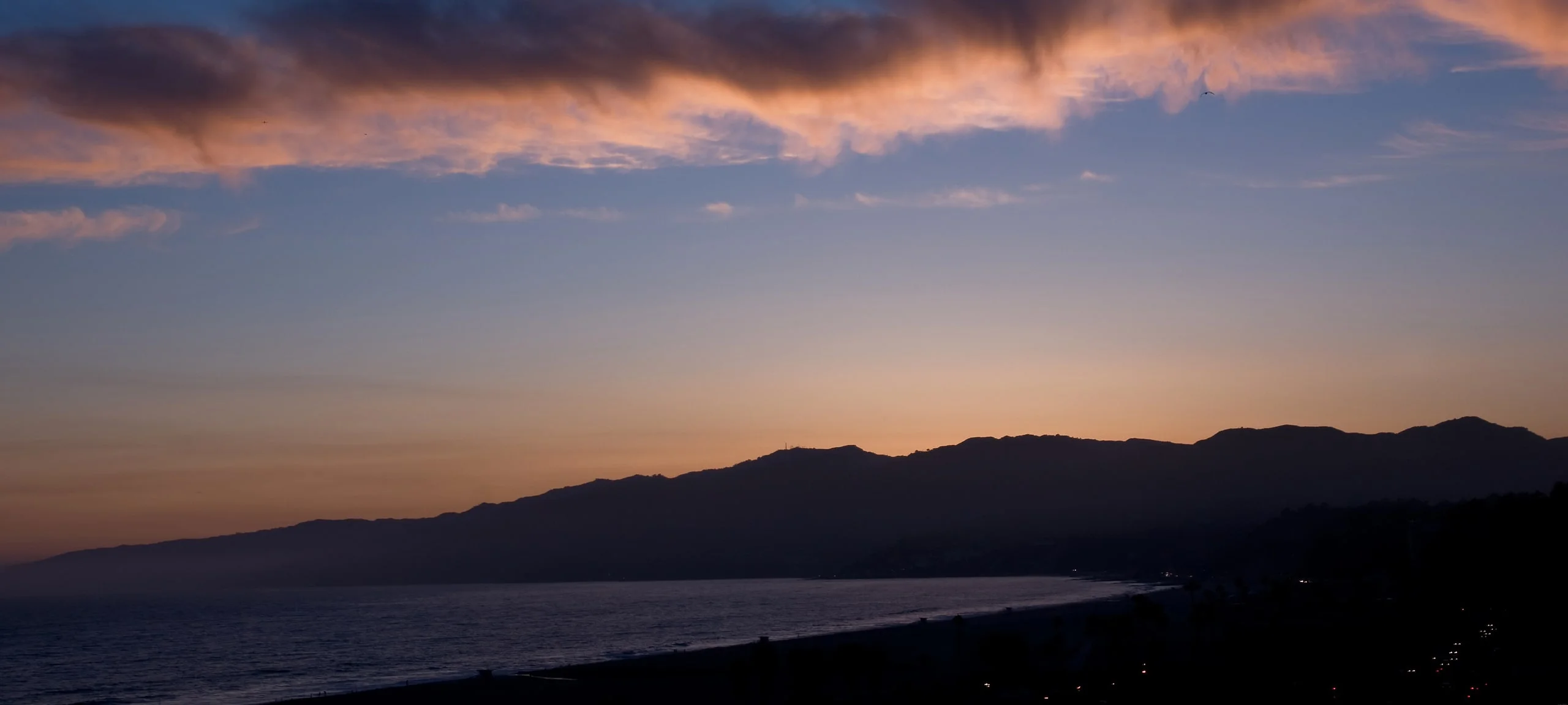 Sunset and silhouette of Qualicum Beach waterfront with lights on hills