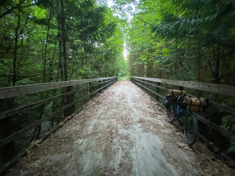 Forest trail with bicycle on one side of a wooden bridge