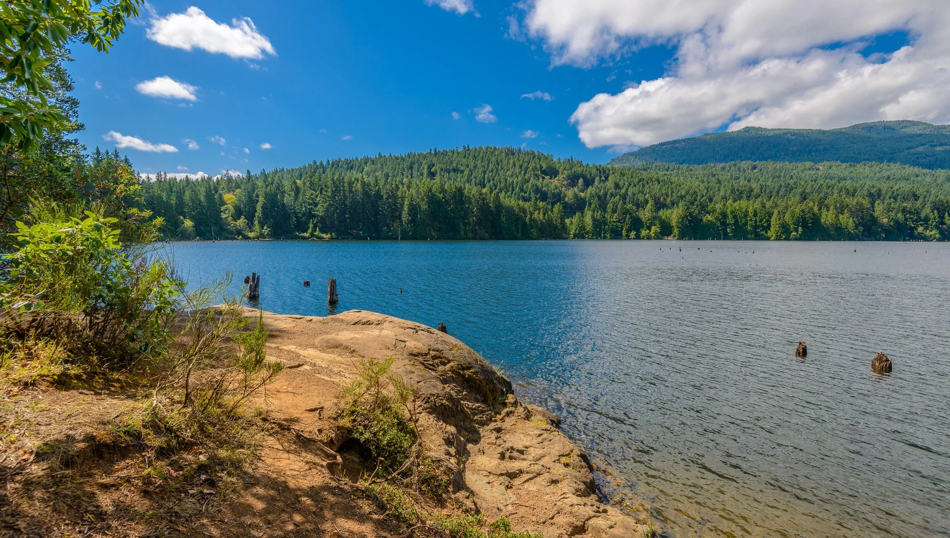 Rocks and Cowichan Lake with mountains in the background on a sunny day